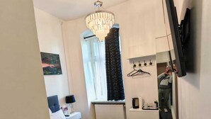 Una camera da letto moderna con un letto, un lampadario, una finestra con tende, un comodino, uno specchio e un televisore montato a parete.