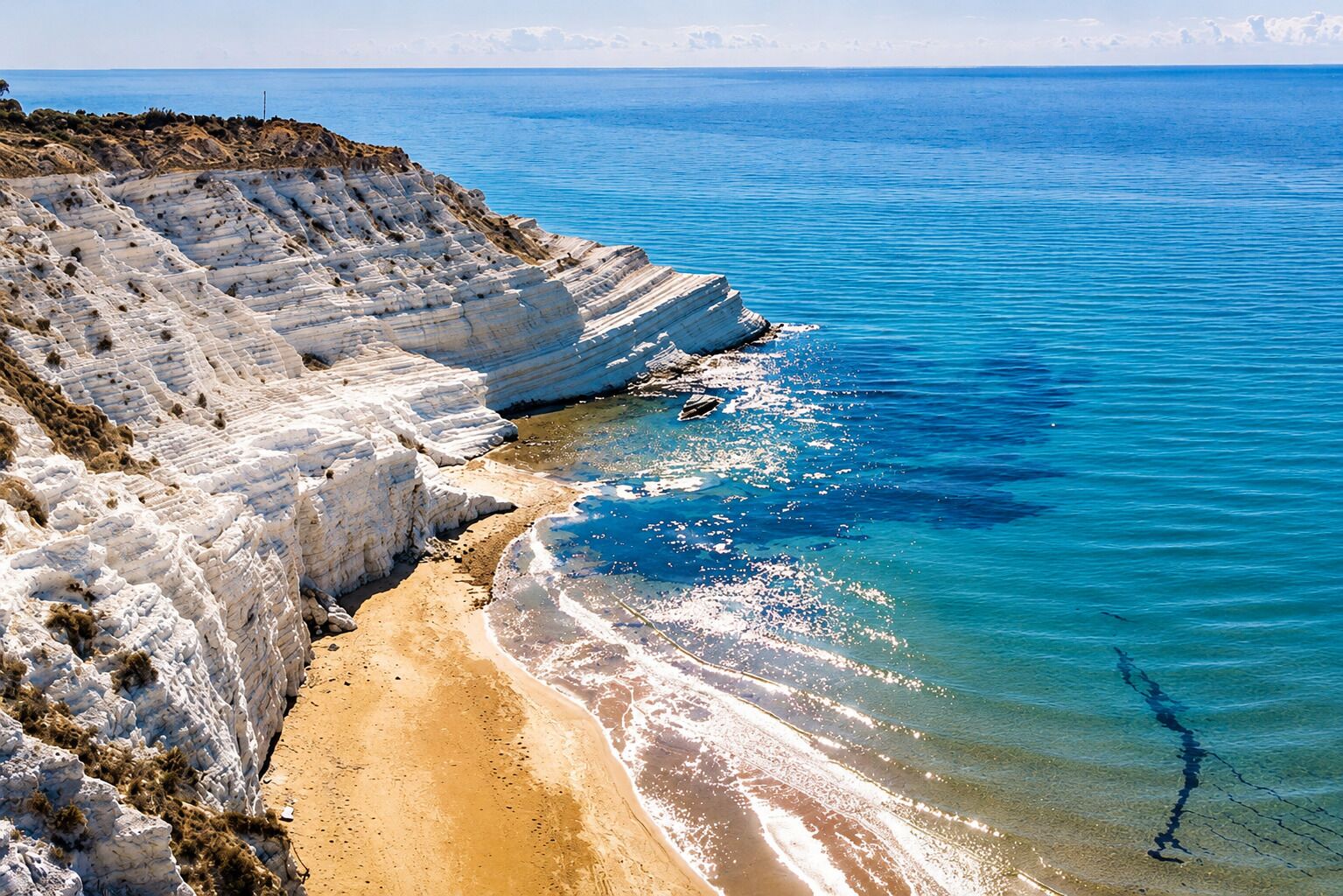 A coastal landscape with white limestone cliffs and a sandy beach.