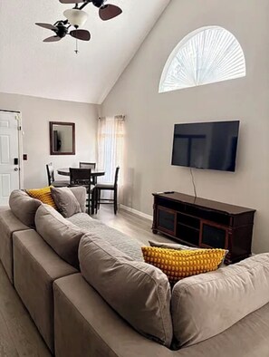 Ein Wohnzimmer mit Sofa, Fernseher, Deckenventilator und Essbereich.