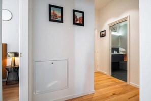 En gang med en hvid dør, et lille bord med en lampe og to billeder i rammer på væggen.