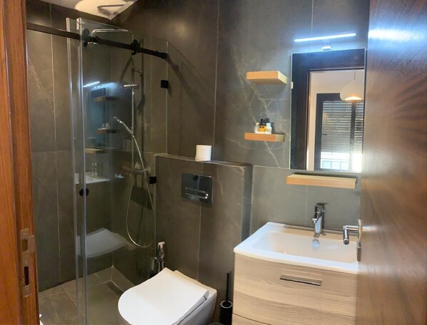 Een moderne badkamer met een glazen douchecabine, een wit toilet, een wastafel met spiegel en een inbouwplank.