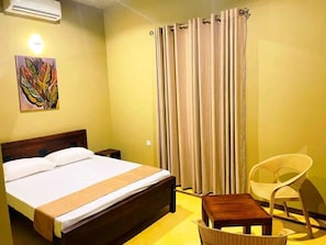 Una habitació d'hotel amb un llit, una cadira, una taula petita i cortines.