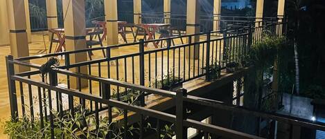 Un espace extérieur abrité, doté d’une rambarde en métal, de jardinières en béton agrémentées de plantes et d’une série de luminaires.