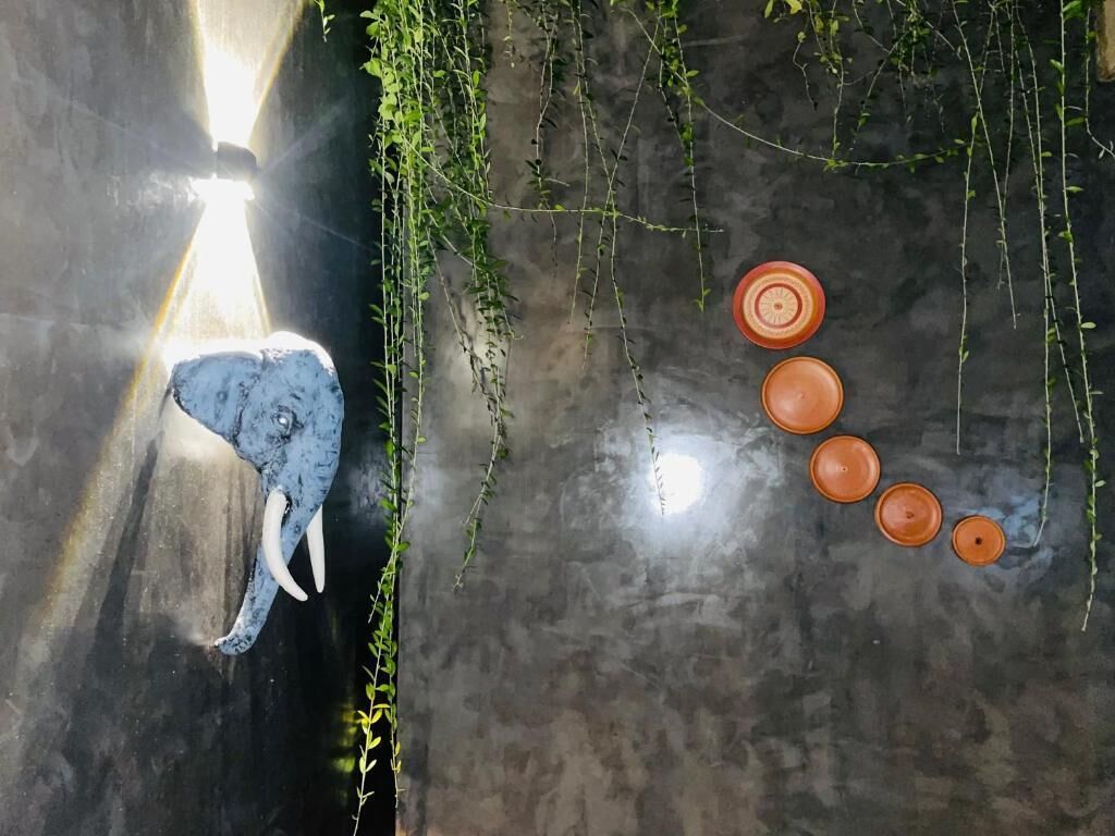 Un sol en béton sur lequel se trouve une sculpture d’un éléphant bleu et quatre pots en terre cuite.