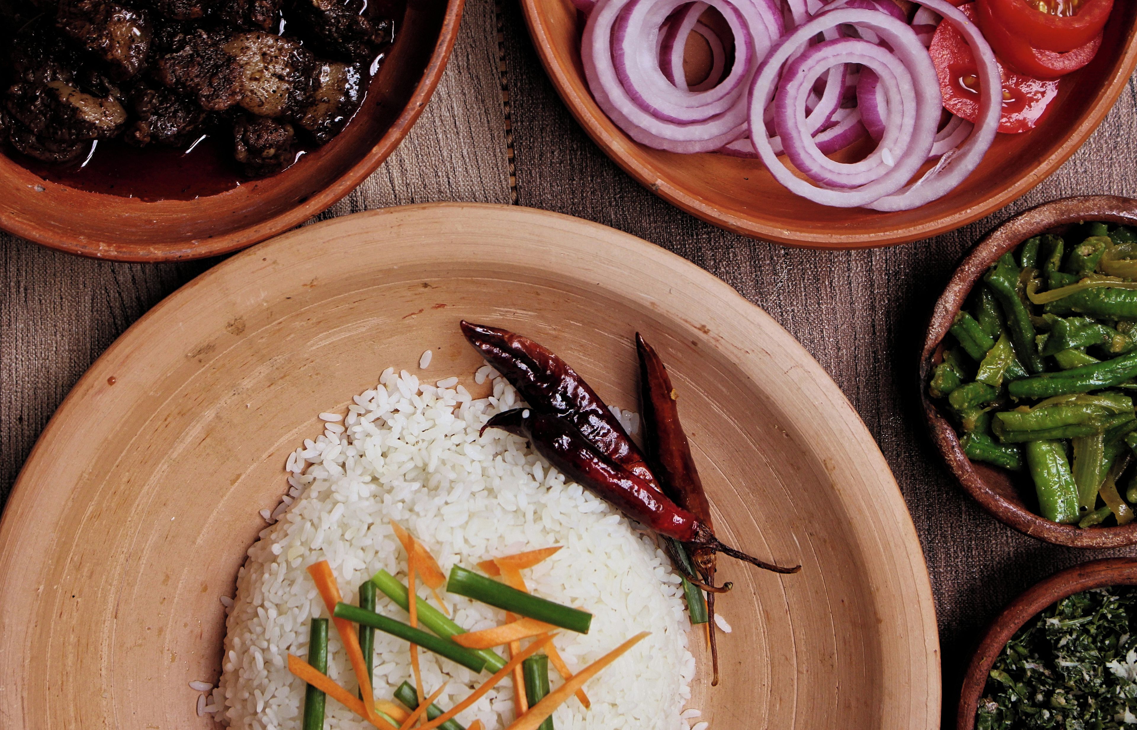 A wooden plate with white rice, green beans, and a red chili pepper.