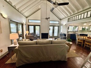 A spacious living room with a large bed, a fireplace, and a dining area with a kitchen in the background.