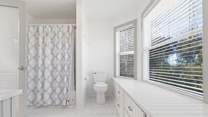 Et badeværelse med toilet, brusekabine og et vindue med persienner.