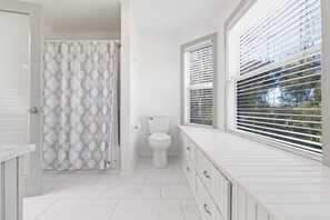 A bathroom with a toilet, a shower curtain, and a window with blinds.