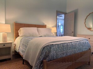 A bedroom with a wooden bed, two bedside tables, a nightstand, a door, and a mirror on the wall.