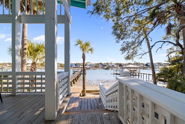 A wooden deck with a white railing overlooking a marina with boats and a beach.