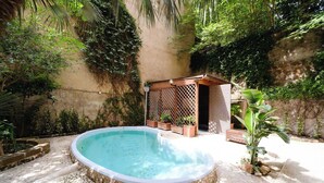 Een hottub omringd door stenen tegels, een houten pergola en weelderige begroeiing.