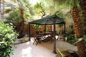 An outdoor patio with a table and chairs, surrounded by tropical plants and a wooden fence. - BuddyRent - Oasi with Private Pool - Trastevere - 6 (Roma)
