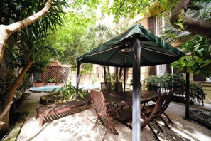 An outdoor patio with a wooden table and chairs, a covered seating area, and a pool in the background. - BuddyRent - Oasi with Private Pool - Trastevere - 6 (Roma)