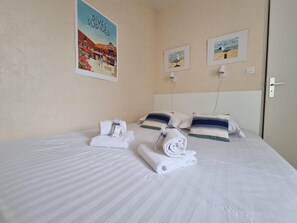 Ein Hotelzimmer mit einem Bett, zwei Kissen, zwei Handtüchern, einer Wandleuchte und zwei gerahmten Bildern.