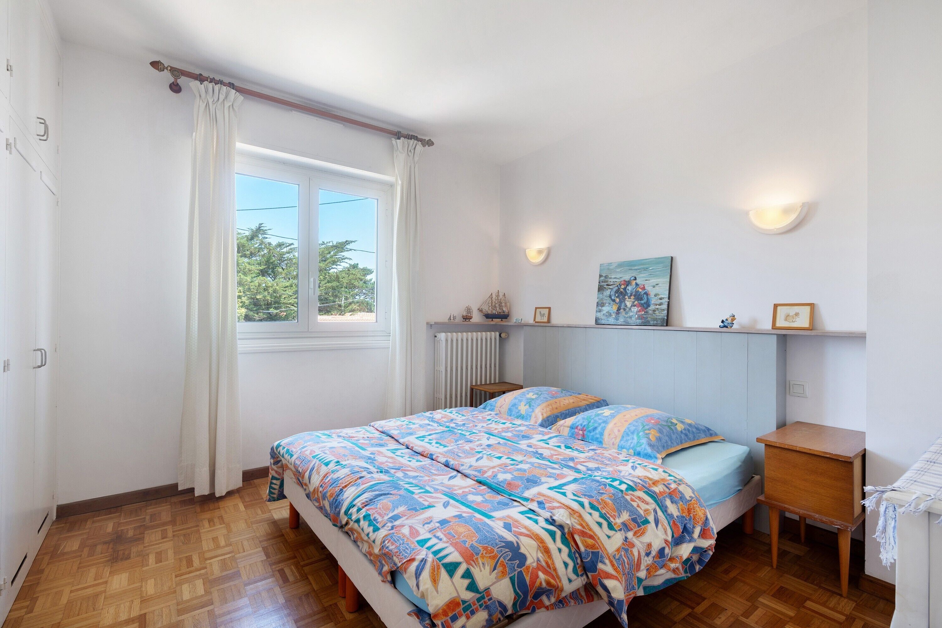 Een slaapkamer met een bed, een raam met gordijnen, een radiator en wandlampen.