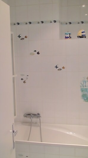 A bathroom with a bathtub, shower, and decorative fish tiles on the wall.