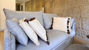 Un sofá gris con cojines estampados frente a una pared de piedra.