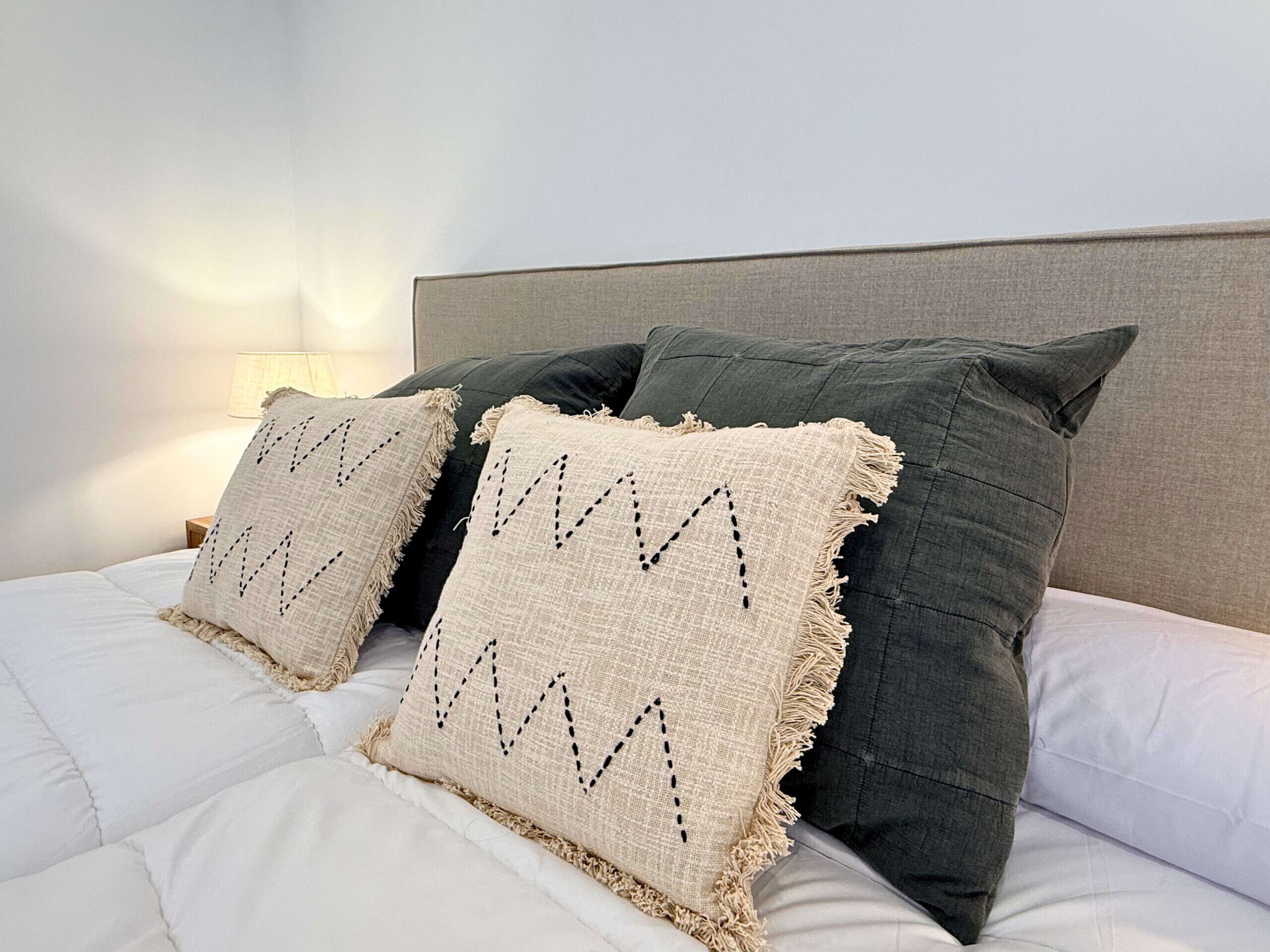 A bed with white bedding, two beige pillows with black zigzag patterns, and a dark green pillow.