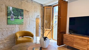 Una sala de estar moderna con una pared de piedra, un sillón amarillo, una mesa redonda de madera, un jarrón blanco, un televisor y un mueble de madera.