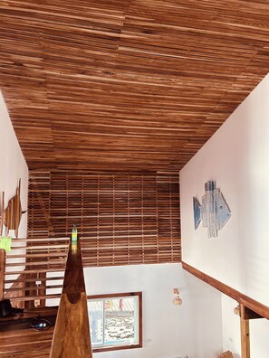 A room with a slatted wooden ceiling, a framed picture on the wall, and a window with a view of the outside.