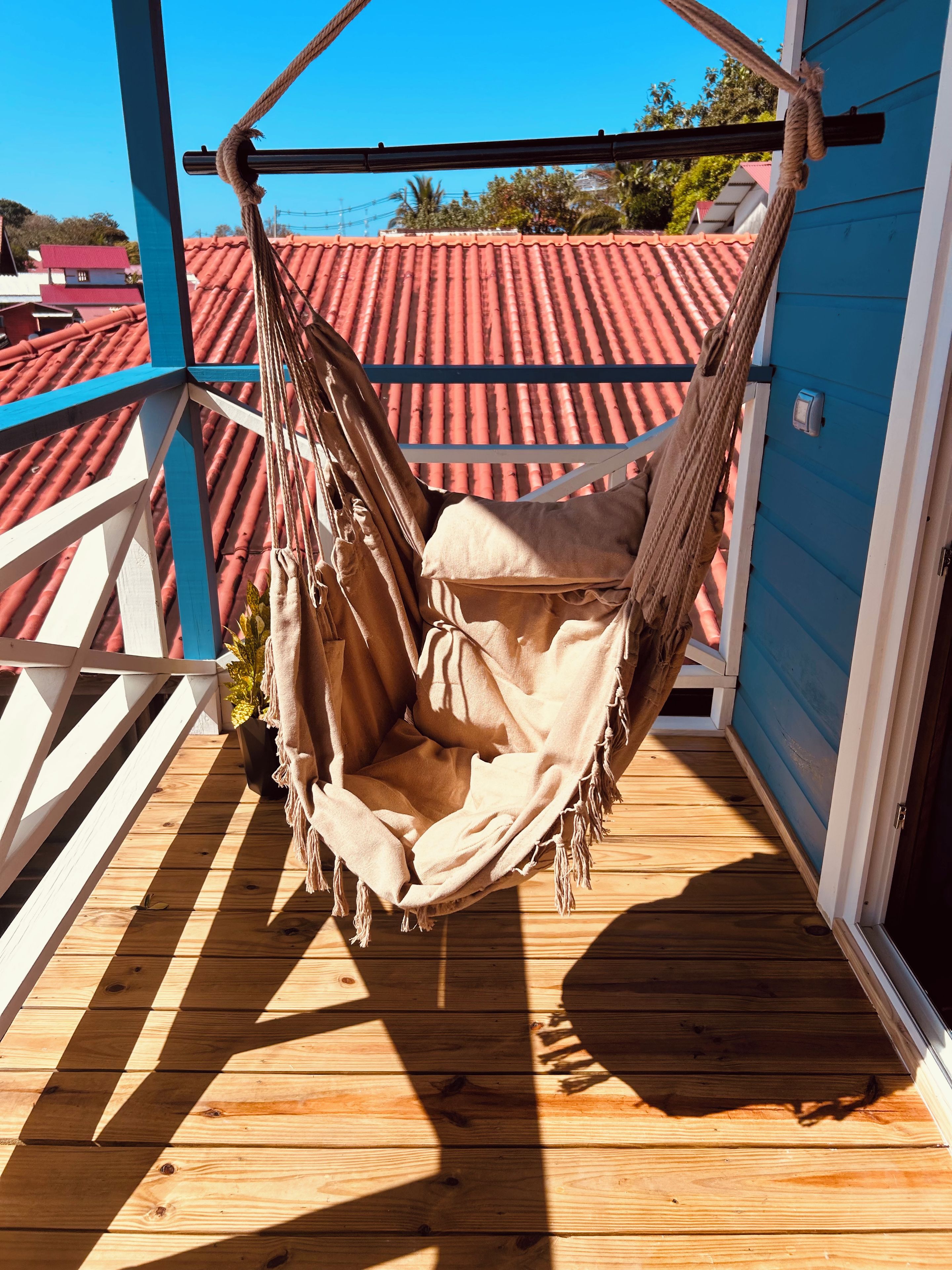 A hammock on a wooden deck with a red-tiled roof in the background.