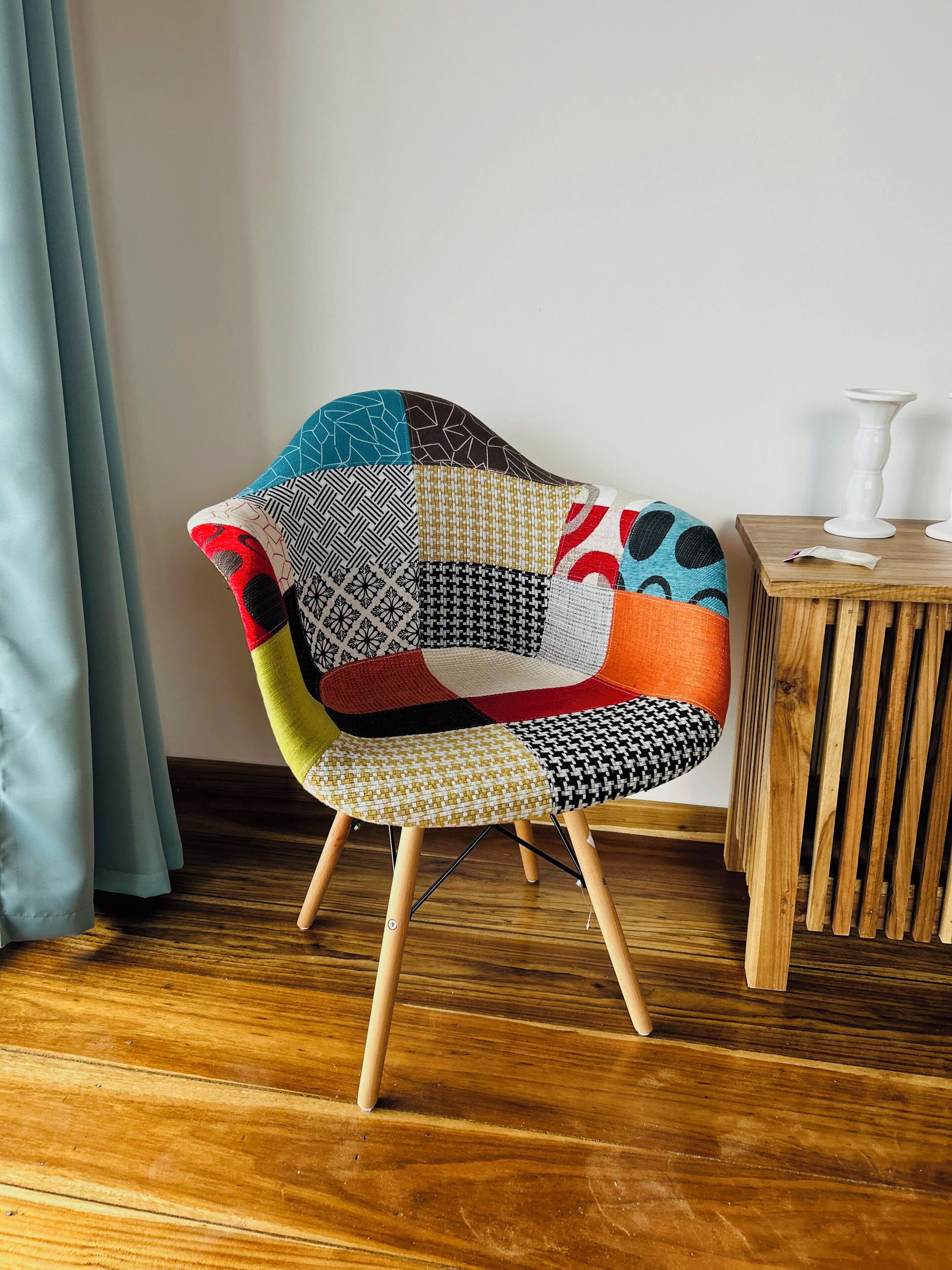Una silla con diseño de retazos, una mesita de madera con una vela blanca y un suelo de madera.