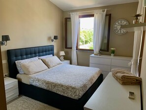 Ein Schlafzimmer mit Bett, Nachttischen, einem Schminktisch, einem Schrank, einem Spiegel, einer Uhr und einem Fenster mit Vorhängen.