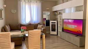 Una sala de estar con un sofá, sillas, un televisor, una mesita y un jarrón decorativo.