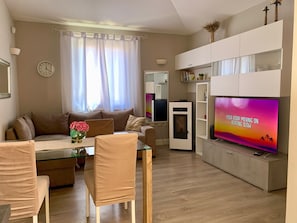 Ein Wohnzimmer mit einer Couch, Sesseln, einem Fernseher, einem kleinen Tisch und einer dekorativen Vase.