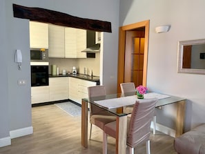 Eine moderne Küche mit weißen Schränken, einer Mikrowelle und einem eingebauten Backofen. Ein Glastisch mit Stühlen, eine Blumenvase und ein Spiegel an der Wand sind ebenfalls vorhanden.