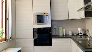 Una cocina con muebles blancos, horno empotrado, microondas, cafetera y lavamanos.