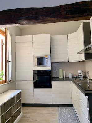 Eine Küche mit weißen Schränken, einem eingebauten Backofen, einer Mikrowelle, einer Kaffeemaschine und einem Spülbecken.