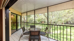 Un balcon fermé avec une table et des chaises, une vue sur un jardin et une porte-fenêtre coulissante.