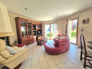 Ein Wohnzimmer mit einer Couch, einem Fernseher, einem Schrank und einer Glastür zum Außenbereich.