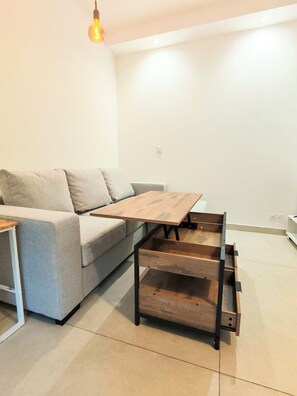 Ein modernes Wohnzimmer mit einem grauen Sofa, einem Couchtisch aus Holz mit Schubladen und einer Pendelleuchte.