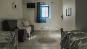 Una habitación con sofá, una mesita redonda, televisor montado en la pared y ventana con cortinas azules.