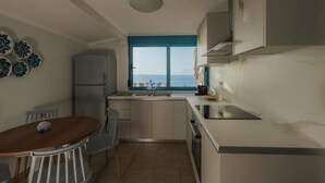 Una cocina compacta con vista al mar, una mesa de comedor con sillas y un refrigerador.