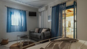 Una habitación con cama, sofá, una mesita, ventana con cortinas, aire acondicionado y vistas por una puerta.
