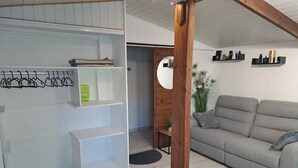 A living room with a grey sofa, wooden beams, white shelving, and a small table with a plant.