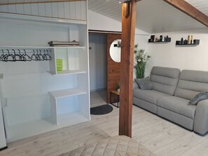 Een woonkamer met een grijze bank, houten balken, witte planken en een kleine tafel met een plant.