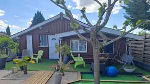 A wooden house with a patio, green lawn, and outdoor seating.