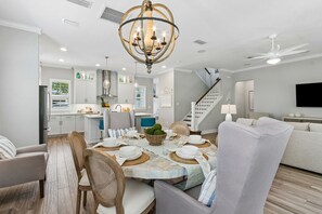 A dining area with a round table set for four, a chandelier, and a staircase leading to another level. - Sunrise on First - Close walk to beach (Fernandina Beach)