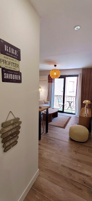 Een moderne woonkamer met houten vloer, een eethoek met tafel en stoelen, een bank, een hanglamp en een balkon met uitzicht.