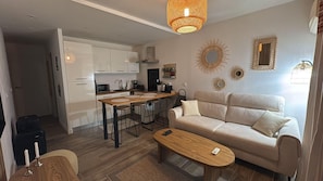 Ein modernes Wohnzimmer mit einer Couch, einem Couchtisch, einer Küchenzeile mit Esstisch und Barhocker sowie dekorativen Wandspiegeln.