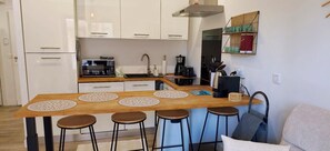Eine moderne Küche mit weißen Schränken, einer Holzeile mit Hockern, einer Kaffeemaschine und einem Einbauofen.