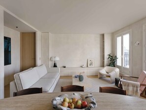 A modern living room with a sofa, armchairs, a coffee table with fruit, a lamp, and a window with a view. - Spacious apartment overlooking the Eiffel Tower (Paris)