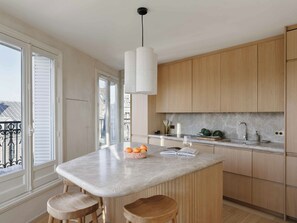 A kitchen with a marble countertop, wooden cabinets, a pendant light, and a view of the outside. - Spacious apartment overlooking the Eiffel Tower (Paris)