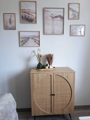 Une pièce avec un meuble en bois, des tableaux encadrés accrochés au mur et une petite table ornée d’objets décoratifs.