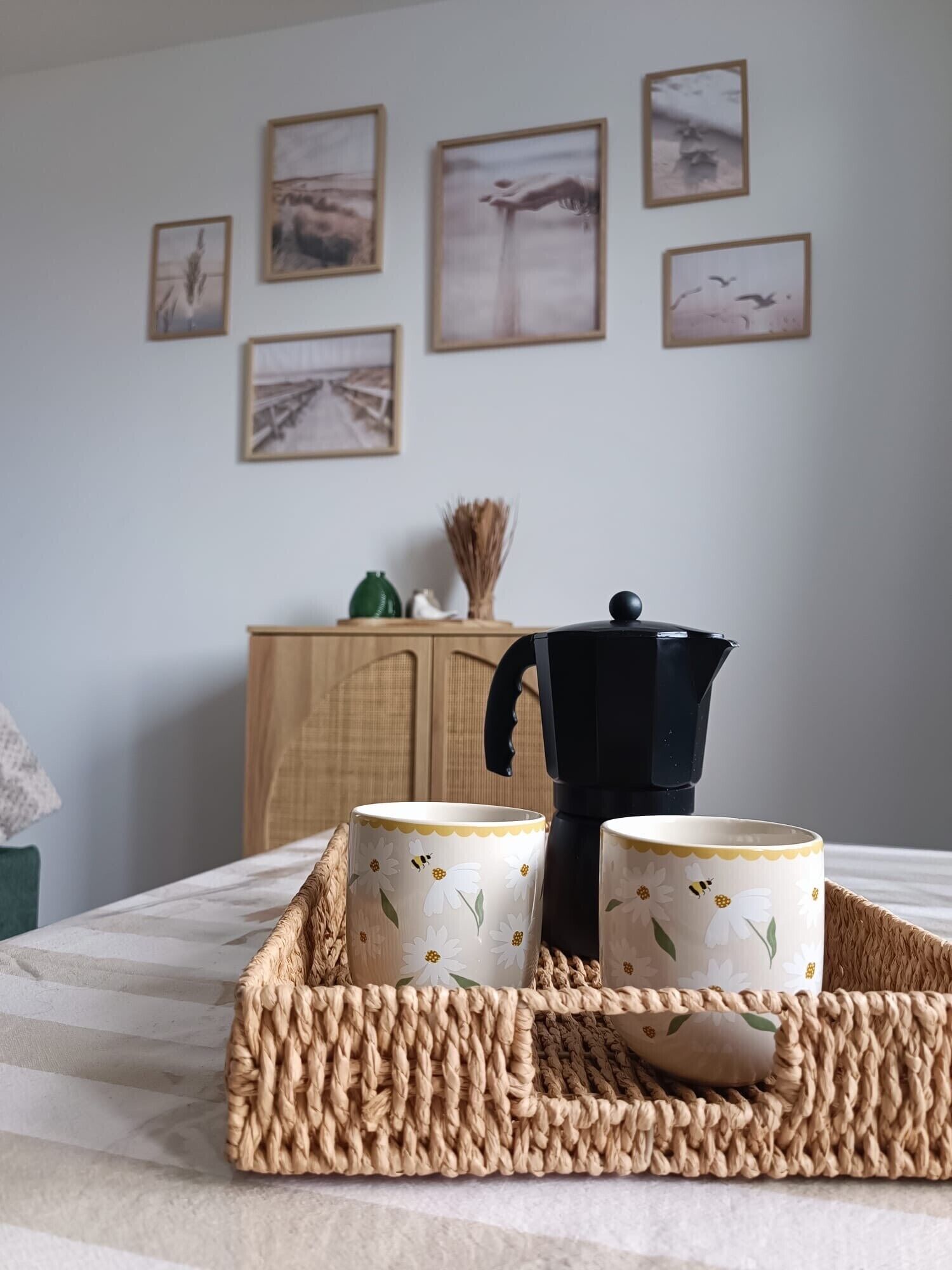 Ein Tablett mit zwei blumengeschmückten Tassen und einer schwarzen Kaffeekanne auf einem Bett.
