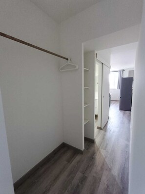 Un couloir doté d’un plancher en bois, de murs blancs et d’un placard avec une tringle en bois et des cintres blancs.